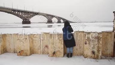 冬天，一个女孩在河边的街道上拍照。 女摄影师在城市的桥边拍照